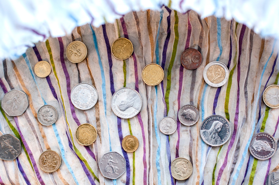 A variety of coins lay on a colourful striped cloth